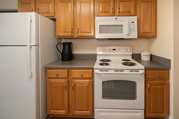 A white refrigerator stands next to a white stove in a kitchen with wooden cabinets.